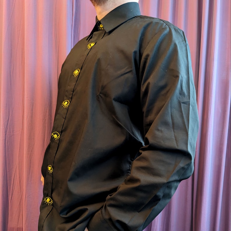 May include: A black long-sleeved button-down shirt with gold eye buttons.