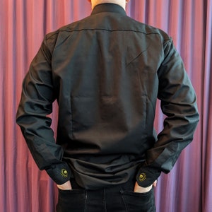 May include: A black long-sleeve shirt with a mock neck collar and gold eye embroidery on the cuffs.