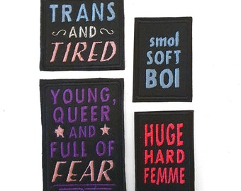 May include: Four black embroidered patches with text. The patches read: "TRANS AND TIRED", "smol SOFT BOI", "YOUNG, QUEER AND FULL OF FEAR", and "HUGE HARD FEMME". The text is in various colors.