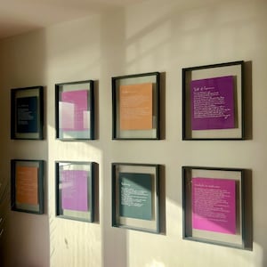 Puede incluir: Ocho marcos flotantes negros cuadrados dispuestos en dos filas sobre una pared. Cada marco contiene una hoja de papel de color con texto impreso en blanco. Los colores incluyen azul oscuro, magenta, naranja y morado, con varios poemas.