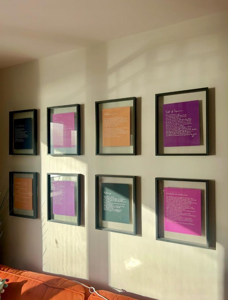 Puede incluir: Ocho marcos flotantes negros cuadrados dispuestos en dos filas sobre una pared. Cada marco contiene una hoja de papel de color con texto impreso en blanco. Los colores incluyen azul oscuro, magenta, naranja y morado, con varios poemas.