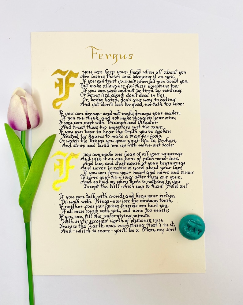 May include: A cream-colored card featuring the poem If by Rudyard Kipling written in black calligraphy with gold illuminated letters. A single artificial tulip with a purple and white flower and green stem sits on the left, and a small turquoise stone is on the bottom right.