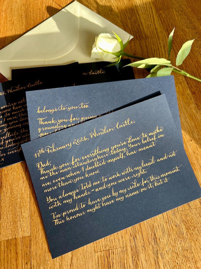 Puede incluir: Una tarjeta azul oscuro con elegante caligraf&iacute;a dorada fechada el 17 de febrero de 2026, Windsor Castle, dirigida a pap&aacute;. La tarjeta se acompa&ntilde;a de un sobre blanco y una rosa blanca, creando un conjunto de papeler&iacute;a formal y sofisticado.