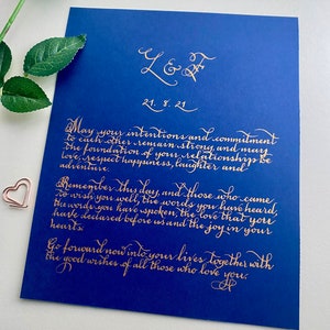 Puede incluir: Una tarjeta rectangular de color azul profundo con elegante caligraf&iacute;a dorada que dice L & F, 21. 8. 21, y un mensaje sincero sobre el compromiso y el amor. Un peque&ntilde;o clip en forma de coraz&oacute;n de oro rosa se encuentra a la izquierda.