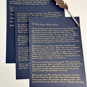 Puede incluir: Tres hojas de papel azul oscuro con texto escrito a mano en tinta dorada, incluyendo el encabezado To My Dear Baby Sister, acompa&ntilde;adas de una pluma de ave marr&oacute;n con punta de metal plateado colocada en diagonal sobre los papeles.