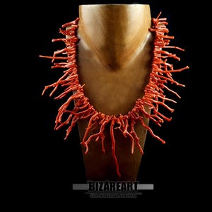 Pu&ograve; includere: Una lunga collana di corallo realizzata con sottili pezzi di corallo ramificati. La collana &egrave; esposta su un manichino di legno su uno sfondo nero.