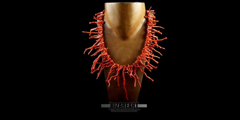 Pu&ograve; includere: Una lunga collana di corallo realizzata con sottili pezzi di corallo ramificati. La collana &egrave; esposta su un manichino di legno su uno sfondo nero.
