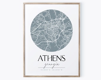 Pode incluir: Uma impressão emoldurada de um mapa de Atenas, Geórgia. O mapa está em um círculo e é de cor azul claro. O texto "Athens, Georgia" e as coordenadas "33.9519° N, 83.3576° W" estão impressas abaixo do mapa.