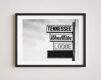 Op de afbeelding: Zwart-wit ingelijste print met een vintage bord voor Tennessee Mountain Lodge. Het bord toont de woorden "TENNESSEE", "Mountain" en "LODGE" in een retro lettertype. De achtergrond toont een bewolkte lucht.