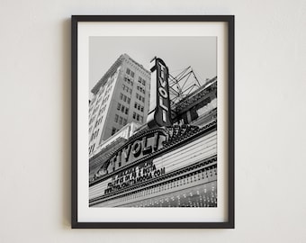 May include: Black and white photograph of a vintage theater marquee with the word "TIVOLI" in large letters. The marquee is lit up with small lights and there is a tall building in the background.