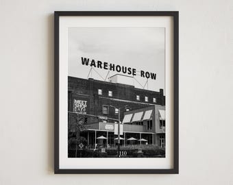 May include: Black and white photograph of a building with a sign that reads "WAREHOUSE ROW". The building has a sign that reads "MEET SHOP EAT" and a sign that reads "1110".