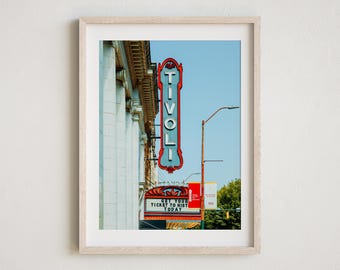 May include: A vintage-style sign for the Tivoli Theater, with red neon lettering on a blue background. The sign is attached to the side of a building with white columns. The sign reads "Get Your Ticket To History Today".