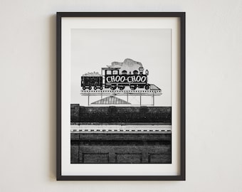 May include: Black and white photograph of a vintage train sign with the words "CHOO-CHOO" on it. The sign is mounted on a building with a brick facade.