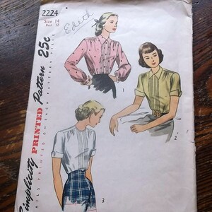 May include: A vintage Simplicity sewing pattern envelope, number 2224, size 14, bust 32. The front features illustrations of three different blouse styles with pleated fronts, short or long sleeves, and various necklines, printed on a white paper background.