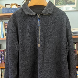 Könnte beinhalten: Ein dunkelgrauer Fleece-Pullover mit einem Viertel-Reißverschluss. Der Reißverschluss hat einen blauen Zipper mit dem aufgedruckten Wort "Timberland".
