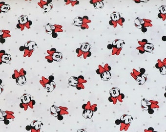 Puede incluir: Tela blanca con un patrón repetido de cabezas de Minnie Mouse rojas y negras con lazos rojos. La tela se mide con una cinta métrica rosa.