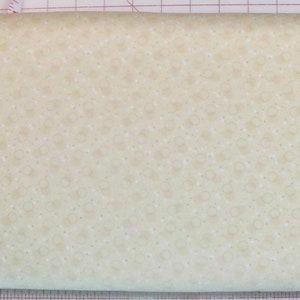 May include: A close-up of a cream-colored fabric with a subtle pattern of small, light brown circles. The fabric is measured with a ruler, showing a length of 43 inches.