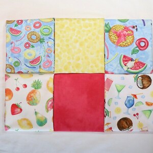 May include: Six fabric squares with different summer-themed patterns. The squares are arranged in a 2x3 grid. The top row features a blue square with white and pink watermelon slices, a yellow square with white polka dots, and a blue square with a pink flamingo and a watermelon slice. The bottom row features a white square with red strawberries, a pink square, and a white square with coconuts and cocktails.