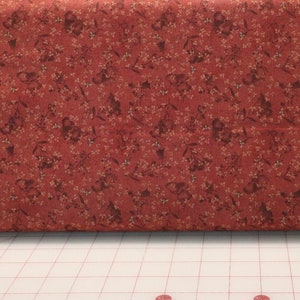 May include: Red fabric with a small white floral pattern. The fabric is folded in half and lying on a white cutting mat with a grid pattern.
