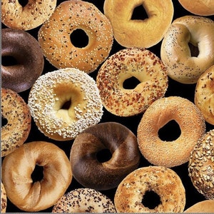 Puede incluir: Primer plano de una variedad de bagels, incluyendo plain, everything, semillas de amapola y sésamo. Los bagels están dispuestos en un patrón aleatorio sobre un fondo negro.