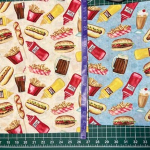 May include: Fabric with a repeating pattern of fast food items. The design includes hamburgers, hot dogs, french fries, ketchup, mustard, and milkshakes. The background is a light beige and light blue. The fabric is approximately 14 inches wide.