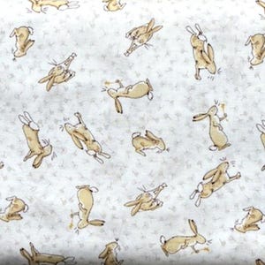 Può includere: Tessuto con un motivo ripetuto di lepri color marrone chiaro in varie pose su sfondo bianco con piccoli accenti floreali grigio chiaro. Le lepri sono raffigurate in uno stile giocoso e a cartoni animati.