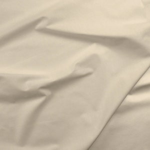 May include: A close-up of a smooth, off-white fabric with a subtle sheen. The fabric is folded and draped, showcasing its texture and drape.