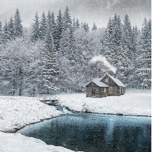 Może przedstawiać: Zimowy krajobraz z ośnieżoną drewnianą chatą otoczoną ośnieżonymi choinkami. Mały mostek przecina strumień. Dym unosi się z komina, a śnieg delikatnie opada.