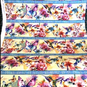 May include: Fabric featuring a watercolor design of butterflies, hummingbirds, and flowers in shades of pink, purple, blue, and yellow. The design is repeated in horizontal stripes with blue borders. Floral and nature themed.