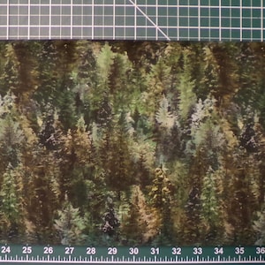 Może przedstawiać: Zbliżenie na tkaninę z nadrukiem lasu. Tkanina jest ciemnobrązowa z zielonymi, beżowymi i białymi drzewami. Tkanina jest mierzona za pomocą fioletowej miarki.