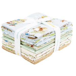 Puede incluir: Un montón de cuadrados de tela atados con una cinta blanca. La tela presenta un fondo azul claro con ilustraciones de animales y otros diseños. La cinta tiene texto impreso. La tela es una mezcla de colores, incluyendo azul, verde y beige.