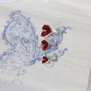 May include: Three red felt heart-shaped charms with silver metal rings. The charms are arranged in descending size order.