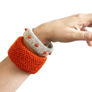 Könnte beinhalten: Zwei gestrickte Armbänder am Handgelenk einer Person. Das untere Armband ist orange und das obere Armband ist beige mit orangefarbenen Punkten.