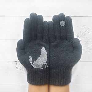 Puede incluir: Un par de guantes de punto grises con un dise&ntilde;o de lobo blanco en un guante y un c&iacute;rculo blanco en el otro.