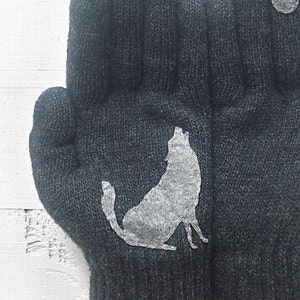 Puede incluir: Un par de guantes de punto grises con un dise&ntilde;o de silueta de lobo blanco. El lobo a&uacute;lla a la luna.