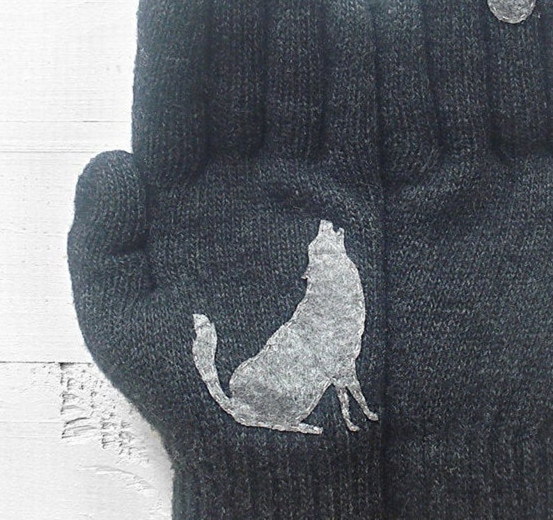 Puede incluir: Un par de guantes de punto grises con un dise&ntilde;o de silueta de lobo blanco. El lobo a&uacute;lla a la luna.