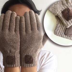 Puede incluir: Un par de guantes de punto marr&oacute;n con parches de cuero en los pu&ntilde;os. Los parches tienen las letras "O" y "L" bordadas.