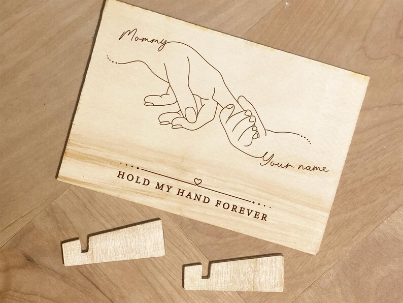 May include: A wooden sign with a line drawing of an adult hand holding a child's hand. The text reads "Mommy" and "Your name" with the phrase "Hold my hand forever" below the drawing.