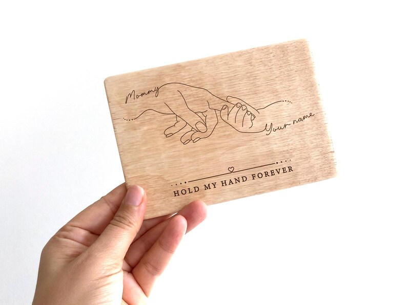 May include: Wooden plaque with a line drawing of two hands holding each other. The text "Mommy" and "Your name" are written above the hands. The text "Hold my hand forever" is written below the hands.