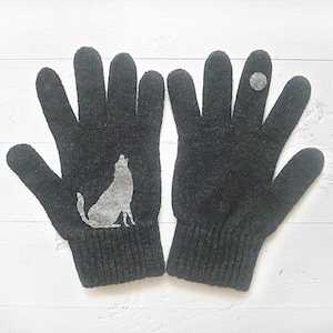 Puede incluir: Un par de guantes de punto grises con una silueta de lobo en un guante y un peque&ntilde;o c&iacute;rculo gris en el otro guante.