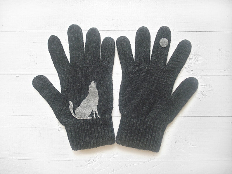 Puede incluir: Un par de guantes de punto grises con una silueta de lobo en un guante y un peque&ntilde;o c&iacute;rculo gris en el otro guante.