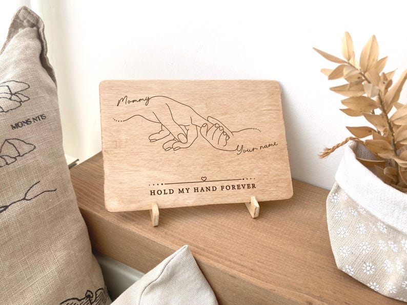 May include: Wooden sign with a hand-drawn illustration of two hands holding each other. The text on the sign reads "Mommy" and "Your name" and "Hold my hand forever".