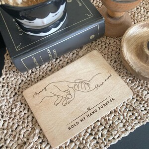 May include: A wooden engraved sign with a line drawing of two hands holding each other. The text reads "Mommy" and "Your name" with the words "Hold my hand forever" below the hands.