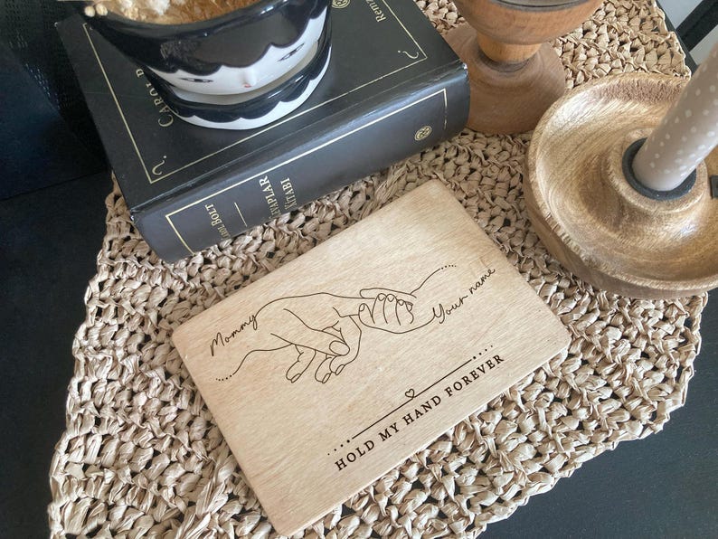 May include: A wooden engraved sign with a line drawing of two hands holding each other. The text reads "Mommy" and "Your name" with the words "Hold my hand forever" below the hands.