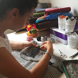 Puede incluir: Una persona est&aacute; cosiendo un parche de tela negro en un su&eacute;ter de punto gris. Hay rollos de fieltro de colores, carretes de hilo y una lata de alfileres de coser en la mesa.