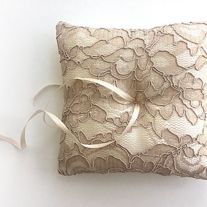 May include: A beige lace ring pillow with a satin ribbon tied around it.
