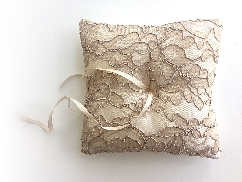 May include: A beige lace ring pillow with a satin ribbon tied around it.