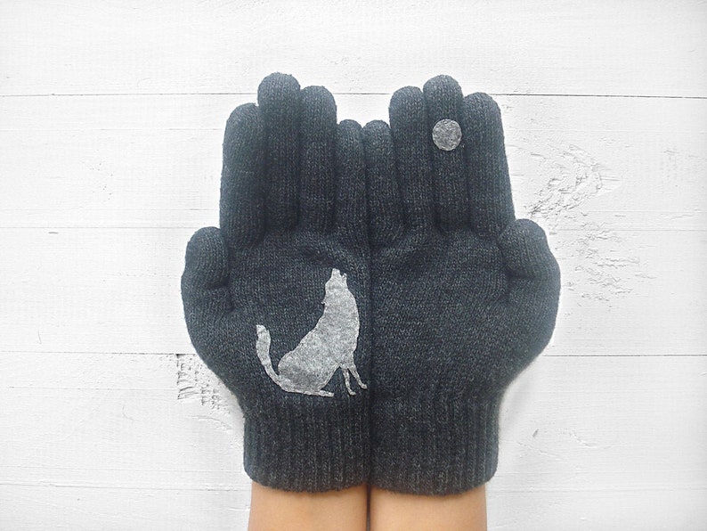 Puede incluir: Un par de guantes de punto grises con un dise&ntilde;o de lobo blanco en un guante y un c&iacute;rculo blanco en el otro.