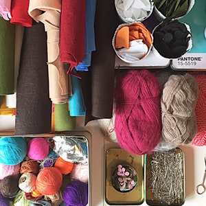 Puede incluir: Una colecci&oacute;n de hilo, fieltro e hilo de colores, incluyendo rosa, rojo, azul, verde y marr&oacute;n. Los materiales est&aacute;n organizados en contenedores y sobre una superficie blanca. La imagen tambi&eacute;n incluye materiales de costura, como tijeras y alfileres.