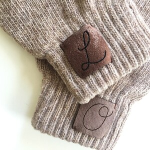 Puede incluir: Dos gorros de punto marr&oacute;n con parches de cuero marr&oacute;n. Los parches tienen las letras "L" y "O" bordadas en hilo negro.
